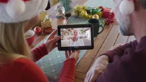 Caucasian-couple-with-santa-hats-using-tablet-for-christmas-video-call-with-woman-on-screen