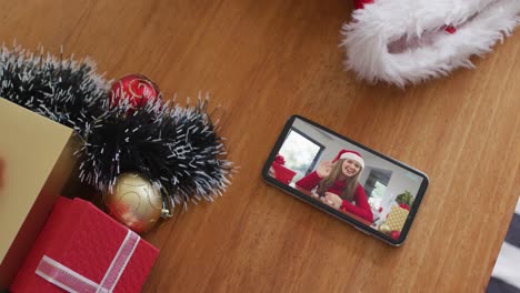 Smiling-caucasian-woman-wearing-santa-hat-on-christmas-video-call-on-smartphone