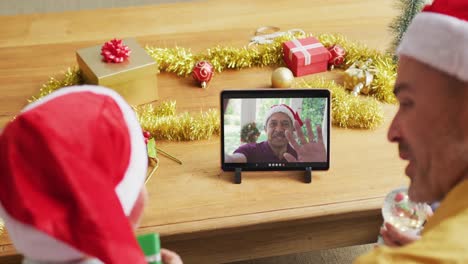 Kaukasischer-Vater-Und-Sohn-Mit-Weihnachtsmützen-Nutzen-Tablet-Für-Weihnachtsvideoanruf-Mit-Mann-Auf-Dem-Bildschirm