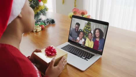 African-american-woman-with-santa-hat-using-laptop-for-christmas-video-call,-with-family-on-screen