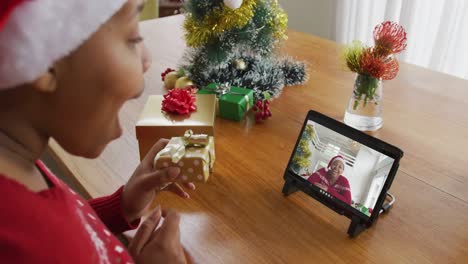 Afroamerikanische-Frau-Mit-Weihnachtsmütze-Nutzt-Tablet-Für-Weihnachtsvideoanruf,-Mit-Freund-Auf-Dem-Bildschirm