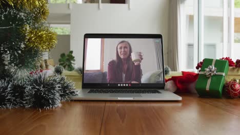 Smiling-caucasian-woman-drinking-coffee-on-christmas-video-call-on-laptop