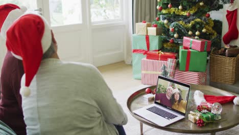 Two-senior-diverse-female-friends-using-laptop-for-christmas-video-call-with-couple-on-screen