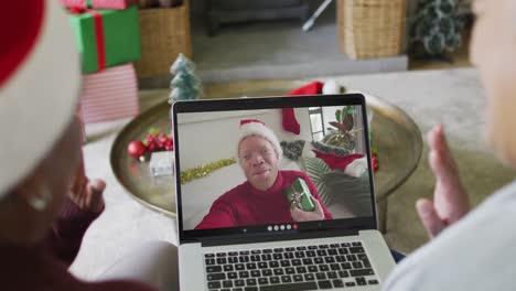 Diverse-senior-female-friends-using-laptop-for-christmas-video-call-with-smiling-man-on-screen