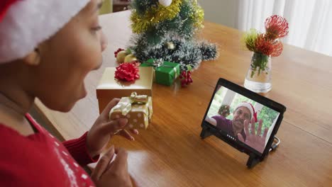 Afroamerikanische-Frau-Mit-Weihnachtsmütze-Nutzt-Tablet-Für-Weihnachtsvideoanruf-Mit-Mann-Auf-Dem-Bildschirm