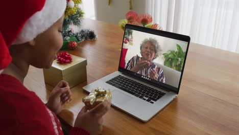 Afroamerikanische-Frau-Mit-Weihnachtsmütze-Nutzt-Laptop-Für-Weihnachtsvideoanruf,-Mit-Frau-Auf-Dem-Bildschirm