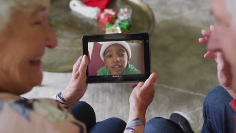 Lächelndes-älteres-Kaukasisches-Paar,-Das-Ein-Tablet-Für-Einen-Weihnachtsvideoanruf-Mit-Einem-Jungen-Auf-Dem-Bildschirm-Verwendet