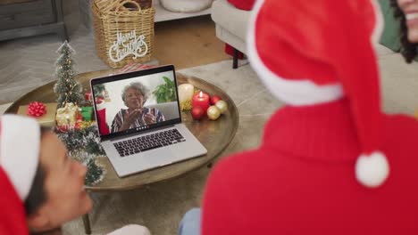 African-american-family-with-santa-hats-using-laptop-for-christmas-video-call-with-woman-on-screen