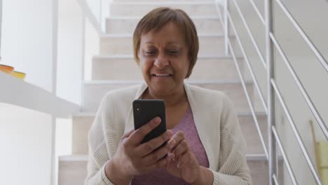 Feliz-Mujer-Mayor-Afroamericana-Sentada-En-Las-Escaleras-Usando-Un-Teléfono-Inteligente-Y-Sonriendo