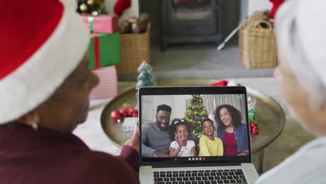 Diverse-senior-female-friends-using-laptop-for-christmas-video-call-with-smiling-family-on-screen