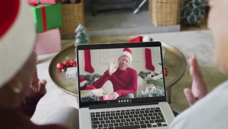 Two-diverse-senior-female-friends-using-laptop-for-christmas-video-call-with-man-on-screen