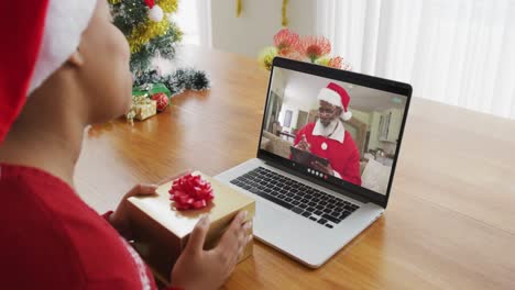 Afroamerikanische-Frau-Mit-Weihnachtsmütze-Nutzt-Laptop-Für-Einen-Weihnachtsvideoanruf-Mit-Dem-Weihnachtsmann-Auf-Dem-Bildschirm