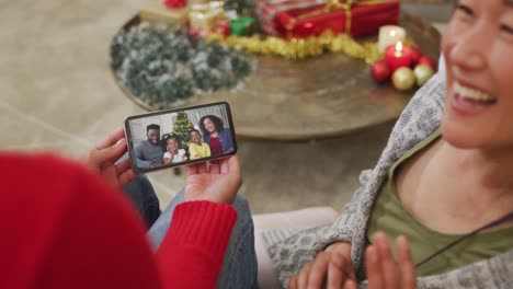 Smiling-asian-couple-using-smartphone-for-christmas-video-call-with-family-on-screen