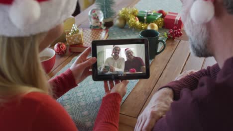 Kaukasisches-Paar-Mit-Weihnachtsmützen-Nutzt-Tablet-Für-Weihnachtsvideoanruf-Mit-Lächelnder-Familie-Auf-Dem-Bildschirm