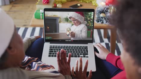 African-american-mother-and-daughter-using-laptop-for-christmas-video-call-with-boy-on-screen
