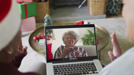 Two-diverse-senior-female-friends-using-laptop-for-christmas-video-call-with-woman-on-screen