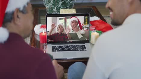 Lächelnder,-Gemischtrassiger-Vater-Und-Sohn,-Die-Einen-Laptop-Für-Einen-Weihnachtsvideoanruf-Mit-Der-Familie-Auf-Dem-Bildschirm-Nutzen