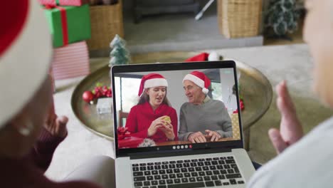 Diverse-senior-female-friends-waving-and-using-laptop-for-christmas-video-call-with-family-on-screen