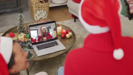 Diverse-family-with-santa-hats-using-laptop-for-christmas-video-call-with-happy-woman-on-screen