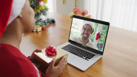 African-american-woman-with-santa-hat-using-laptop-for-christmas-video-call,-with-man-on-screen