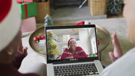 Verschiedene-ältere-Freundinnen-Winken-Und-Benutzen-Laptop-Für-Einen-Weihnachtsvideoanruf-Mit-Einer-Frau-Auf-Dem-Bildschirm