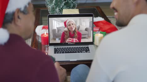 Smiling-biracial-father-and-son-using-laptop-for-christmas-video-call-with-woman-on-screen