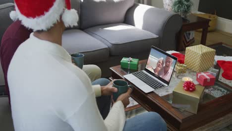 Biracial-father-and-son-using-laptop-for-christmas-video-call-with-happy-couple-on-screen