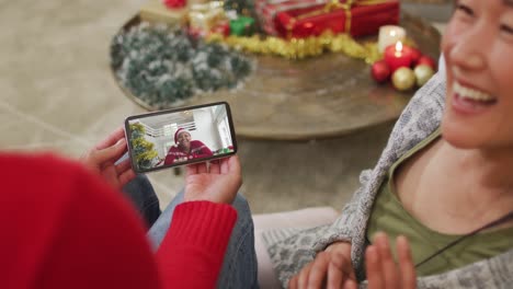 Smiling-asian-couple-using-smartphone-for-christmas-video-call-with-woman-on-screen