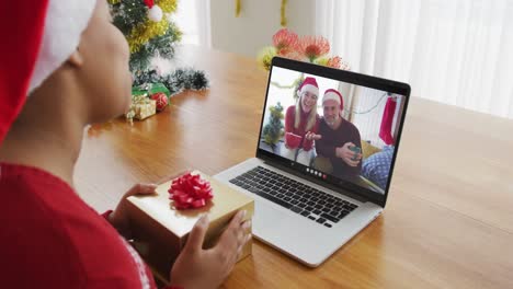 Afroamerikanische-Frau-Mit-Weihnachtsmütze-Nutzt-Laptop-Für-Weihnachtsvideoanruf,-Mit-Paar-Auf-Dem-Bildschirm