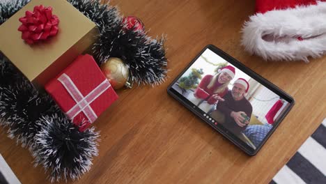 Smiling-caucasian-father-with-daughter-wearing-santa-hats-on-christmas-video-call-on-tablet