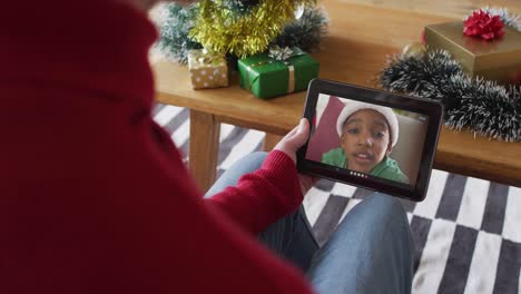 Caucasian-man-using-tablet-and-waving-for-christmas-video-call-with-smiling-boy-on-screen