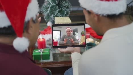 Biracial-father-and-son-waving-and-using-tablet-for-christmas-video-call-with-smiling-man-on-screen