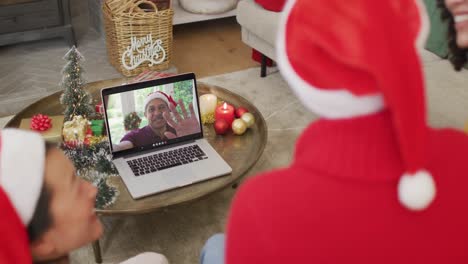 Afroamerikanische-Familie-Mit-Weihnachtsmützen-Nutzt-Laptop-Für-Weihnachtsvideoanruf-Mit-Mann-Auf-Dem-Bildschirm