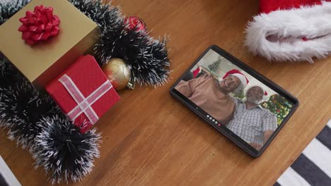 Smiling-african-american-senior-couple-with-santa-hats-on-christmas-video-call-on-tablet