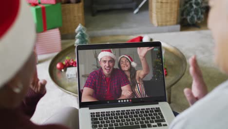 Diverse-senior-female-friends-waving-and-using-laptop-for-christmas-video-call-with-couple-on-screen