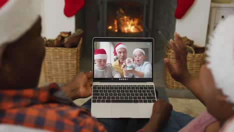 African-american-couple-with-santa-hats-using-laptop-for-christmas-video-call-with-family-on-screen