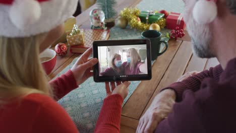 Kaukasisches-Paar-Mit-Weihnachtsmützen-Nutzt-Tablet-Für-Weihnachtsvideoanruf-Mit-Der-Familie-Auf-Dem-Bildschirm