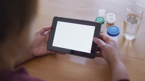 Afroamerikanische-Seniorin-Hält-Tablet-Mit-Kopierplatz-Auf-Dem-Bildschirm,-Medikamentenflaschen-Auf-Dem-Tisch
