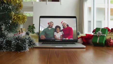 Smiling-african-american-family-wearing-santa-hats-on-christmas-video-call-on-laptop