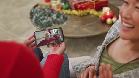 Smiling-asian-couple-using-smartphone-for-christmas-video-call-with-man-with-santa-hat-on-screen