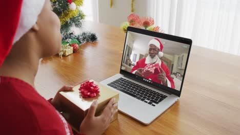 African-american-woman-with-santa-hat-using-laptop-for-christmas-video-call-with-santa-on-screen
