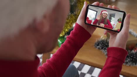 Kaukasischer-Mann-Mit-Weihnachtsmütze-Nutzt-Smartphone-Für-Weihnachtsvideoanruf-Mit-Lächelnder-Frau-Auf-Dem-Bildschirm