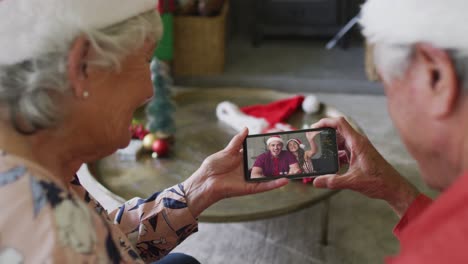 Smiling-senior-caucasian-couple-using-smartphone-for-christmas-video-call-with-couple-on-screen