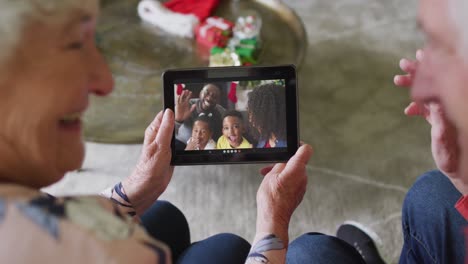 Smiling-caucasian-senior-couple-using-tablet-for-christmas-video-call-with-family-on-screen