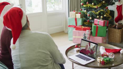 Diverse-senior-female-friends-waving-and-using-laptop-for-christmas-video-call-with-man-on-screen