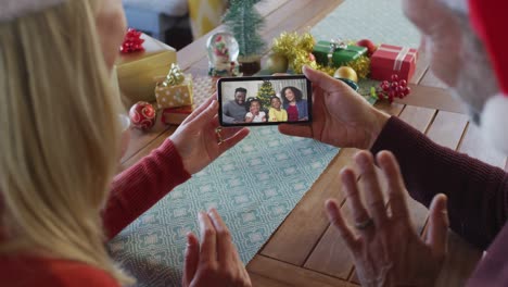 Caucasian-couple-with-santa-hats-using-smartphone-for-christmas-video-call-with-family-on-screen