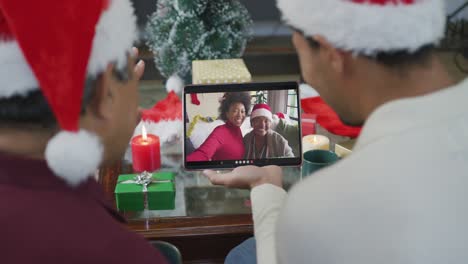 Biracial-father-and-son-waving-and-using-tablet-for-christmas-video-call-with-happy-family-on-screen