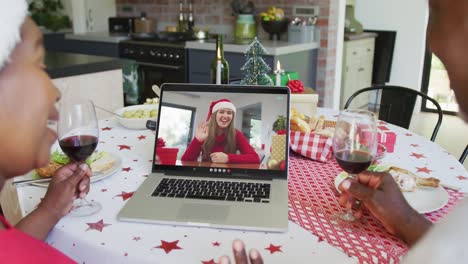 Smiling-african-american-couple-with-wine-using-laptop-for-christmas-video-call-with-woman-on-screen