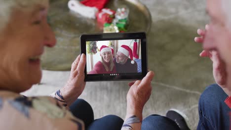 Lächelndes-älteres-Kaukasisches-Paar,-Das-Ein-Tablet-Für-Einen-Weihnachtsvideoanruf-Mit-Einem-Paar-Auf-Dem-Bildschirm-Verwendet