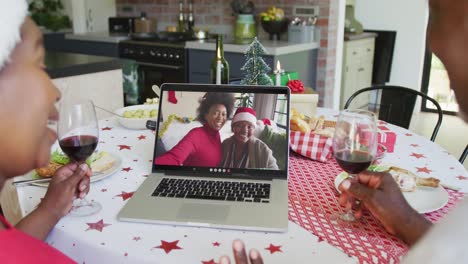 African-american-couple-with-wine-using-laptop-for-christmas-video-call-with-family-on-screen